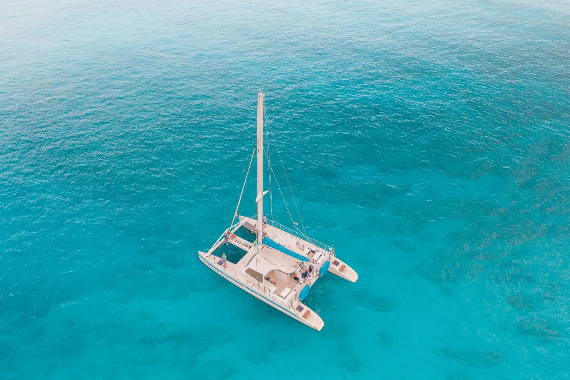 A sailing catamaran anchored in a turquoise bay on the Athens Riviera with swimmers in the water