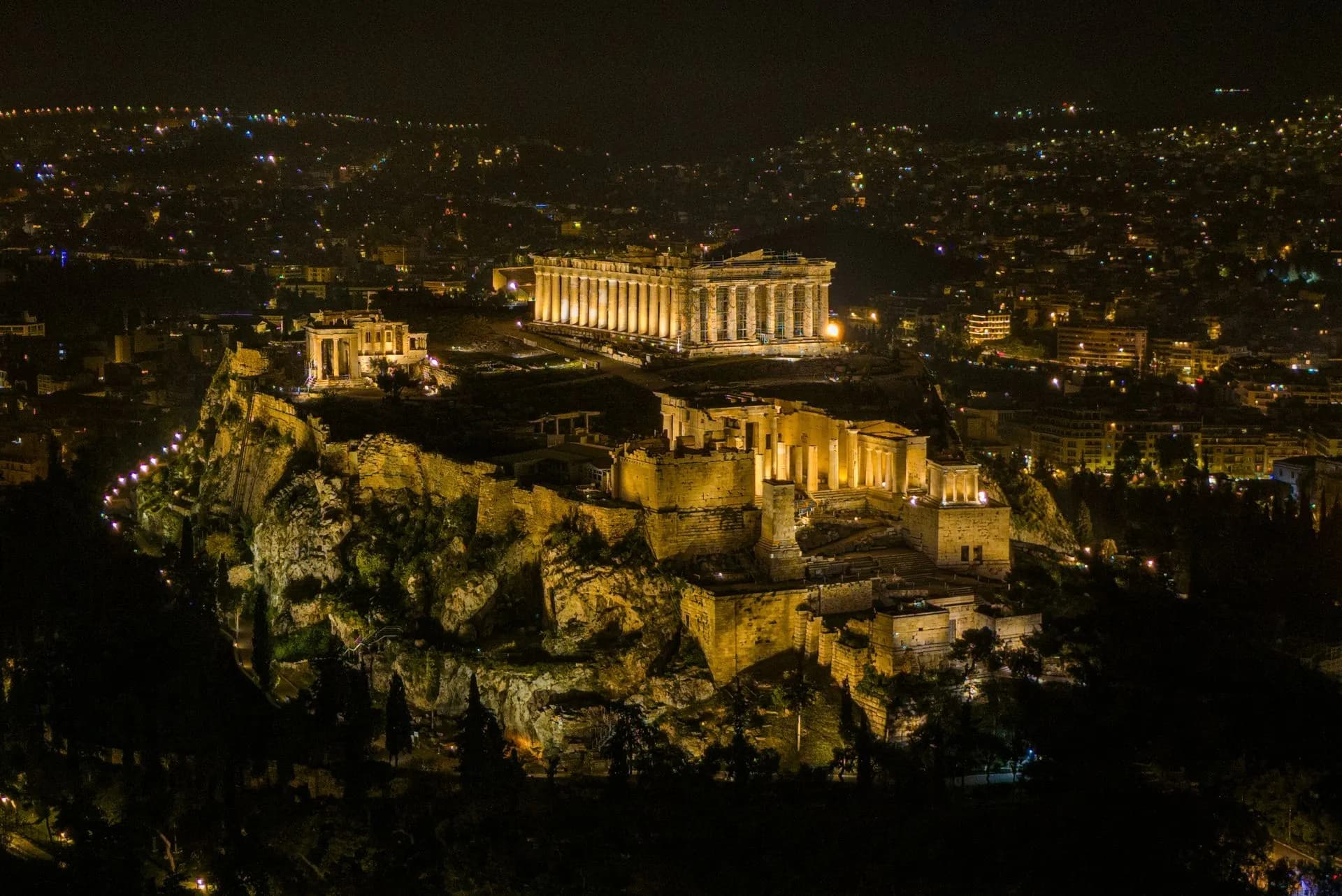 The floodlit Parthenon glowing above the rooftops of Plaka on a deep blue Athens evening