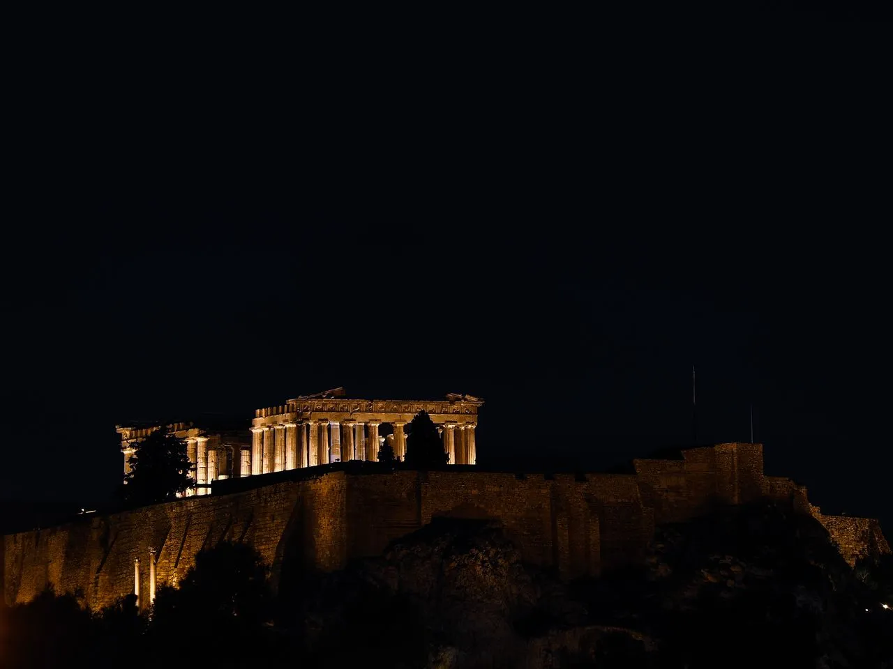 The floodlit Parthenon glowing against a dark sky above Athens