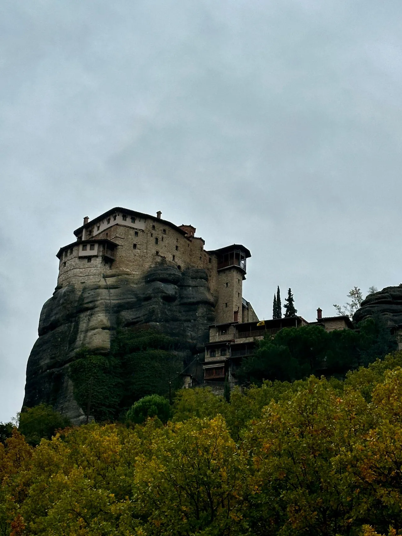 A Meteora monastery perched on a sandstone pillar above green forest near Kalambaka, Greece